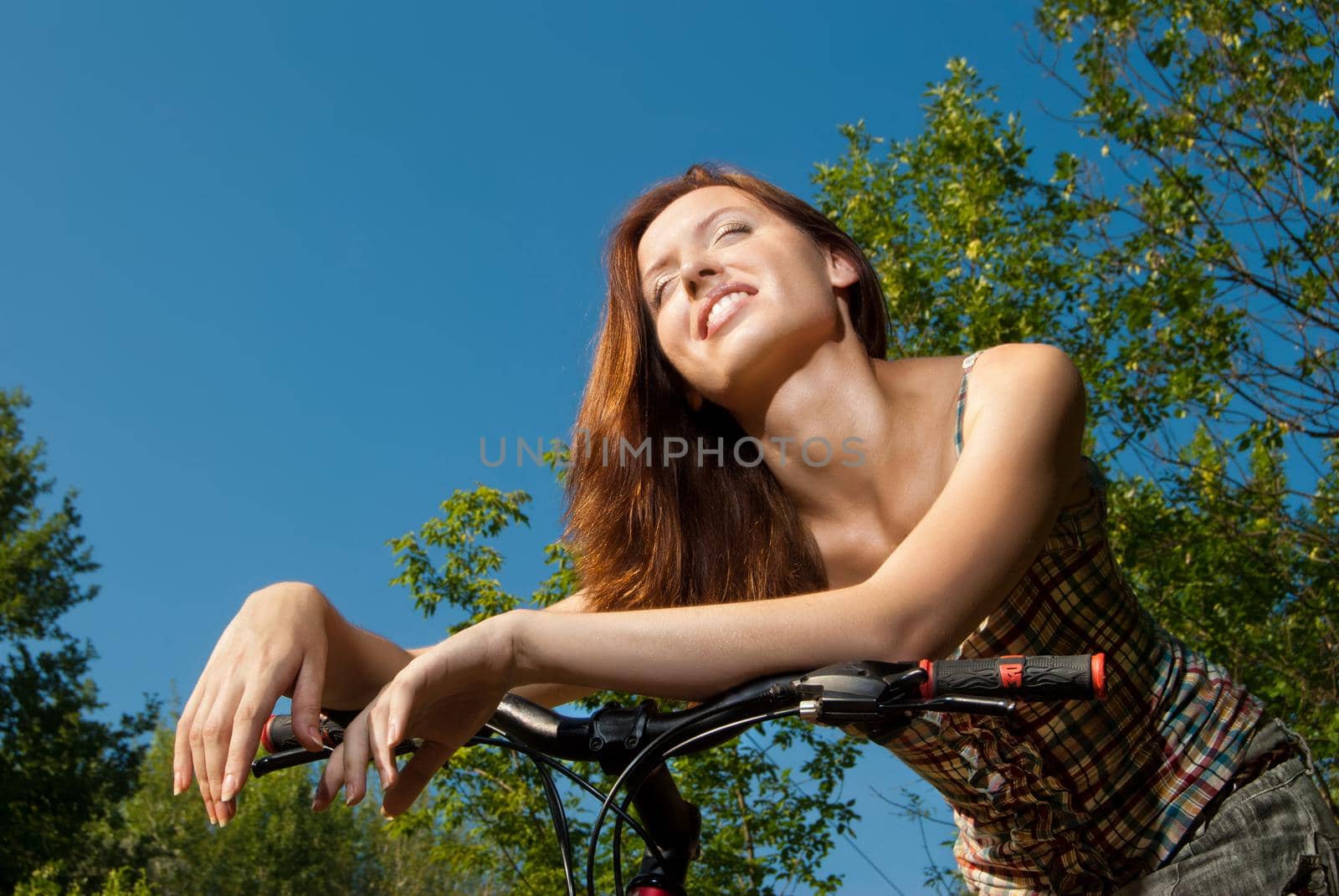 Portrait of pretty young woman with bicycle in a park smiling - Outdoor