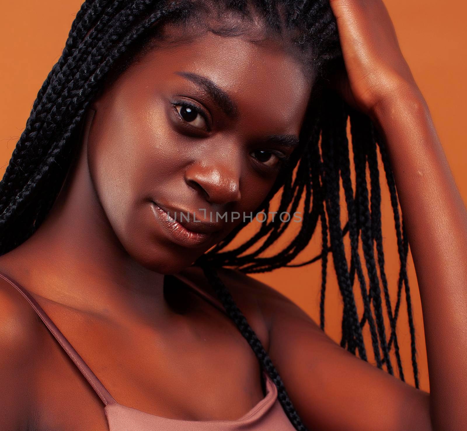 pretty young african american woman with braids posing cheerful gesturing on brown background, lifestyle people concept close up