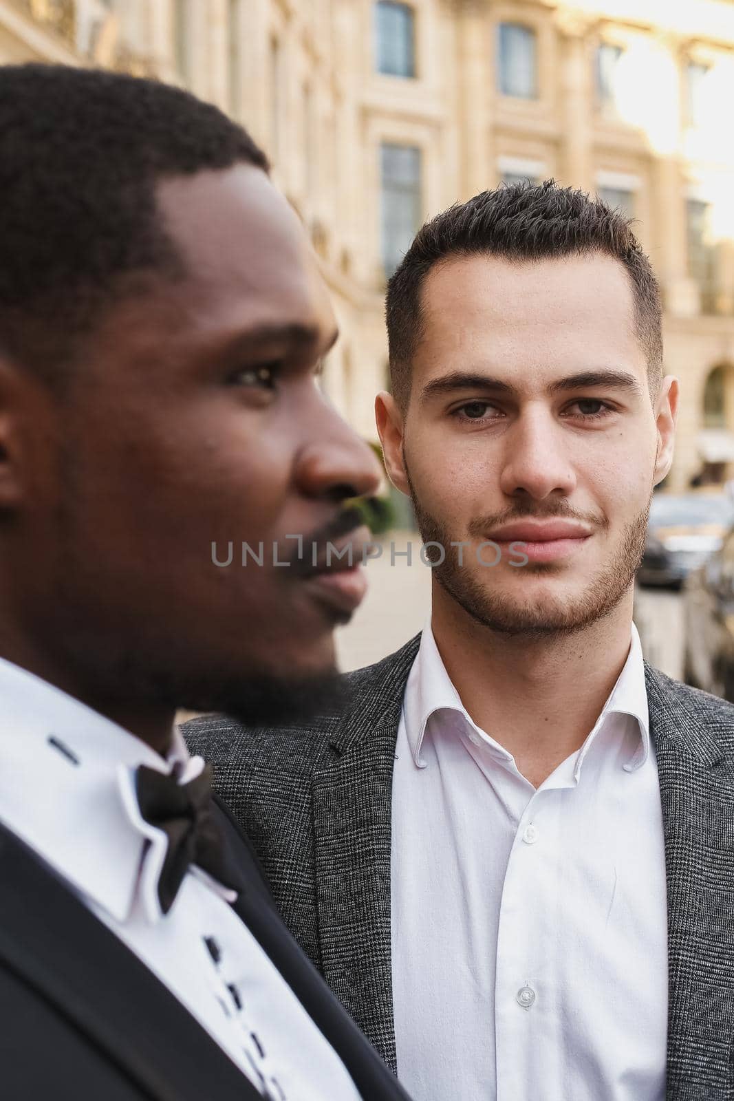 close up portrait of same sex couple. caucasian man wearing suit standing near afro american boy. Concept of business and male fashion.