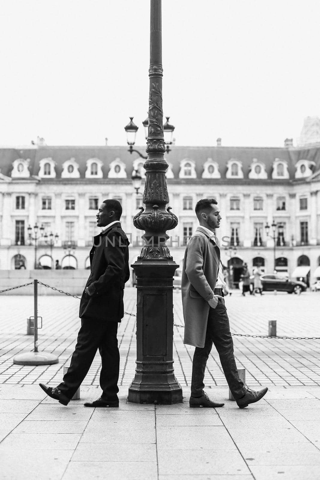 Black and white photo of afro american and caucasian boys standing near street lantern, wearing suits. Concept of urban photo session and life style.