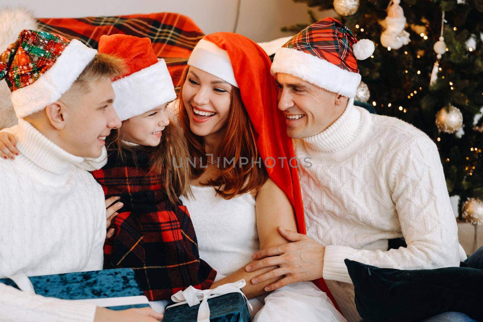 Close-up portrait of a happy family sitting on a sofa near a Christmas tree celebrating a holiday by Lobachad