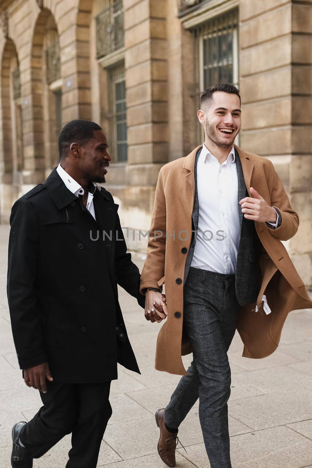 Caucasian smiling man in suit walking with afroamerican male person and hugging in city. Concept of happy lgbt gay and strolling.