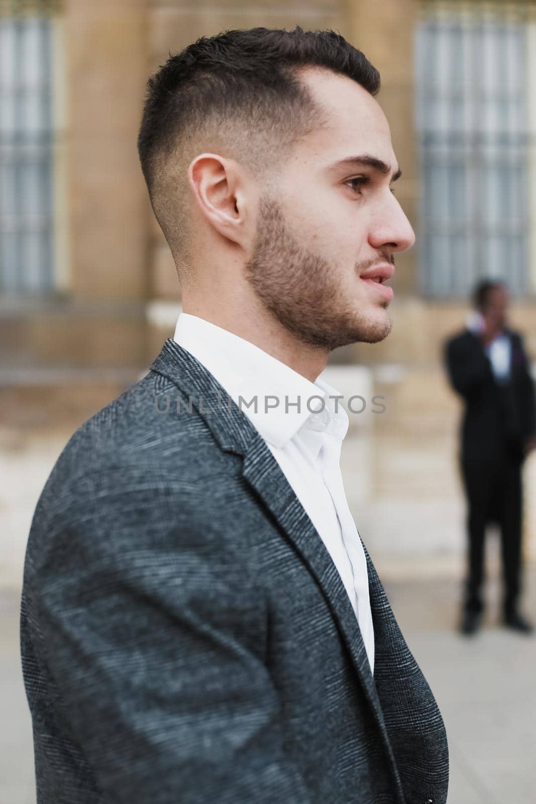 Young cacuasian man wearing suit standing near building outside. by sisterspro