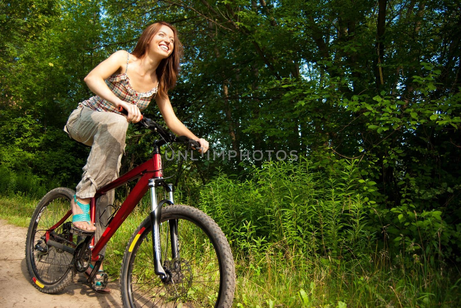 Pretty young woman with bicycle in a park smiling by Julenochek