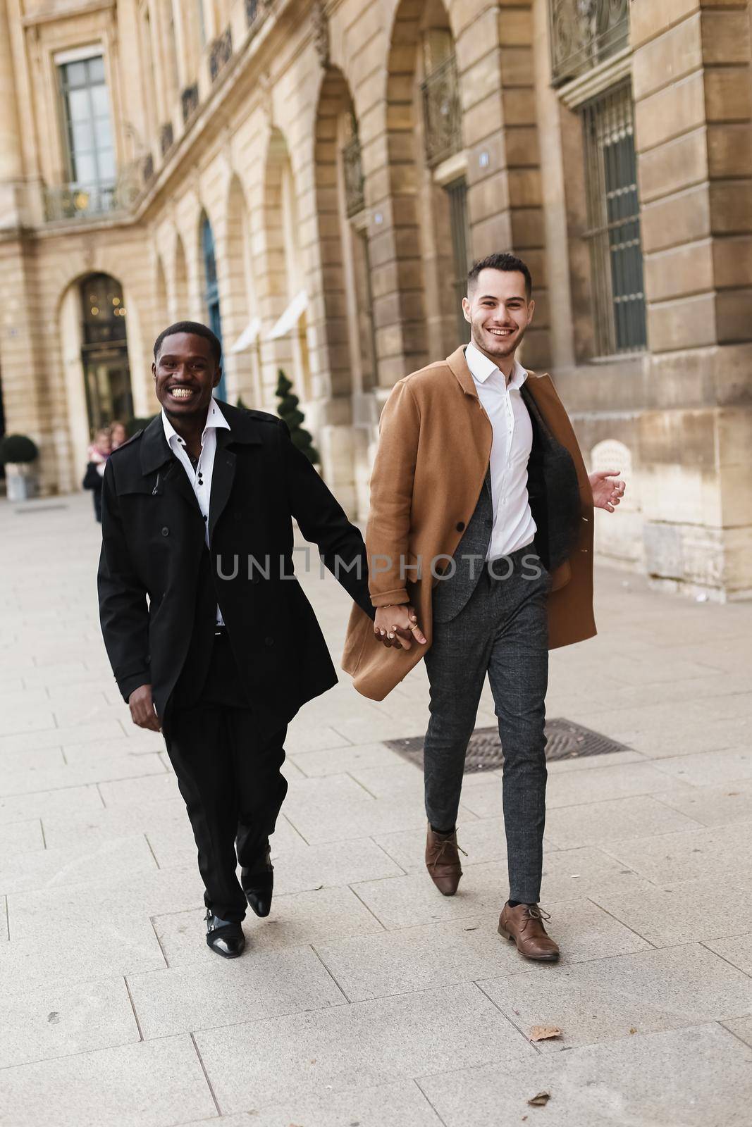 Caucasian smiling man in suit walking with afroamerican male person and hugging in city. Concept of happy lgbt gay and strolling.