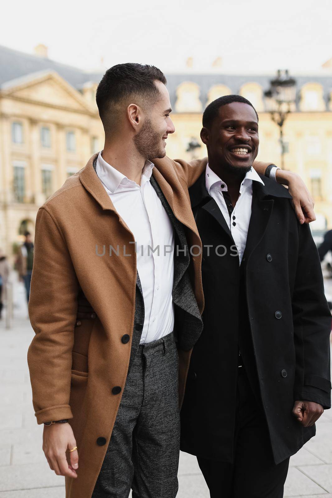 Caucasian smiling man in suit walking with afroamerican male person and hugging in city. Concept of happy lgbt gay and strolling.