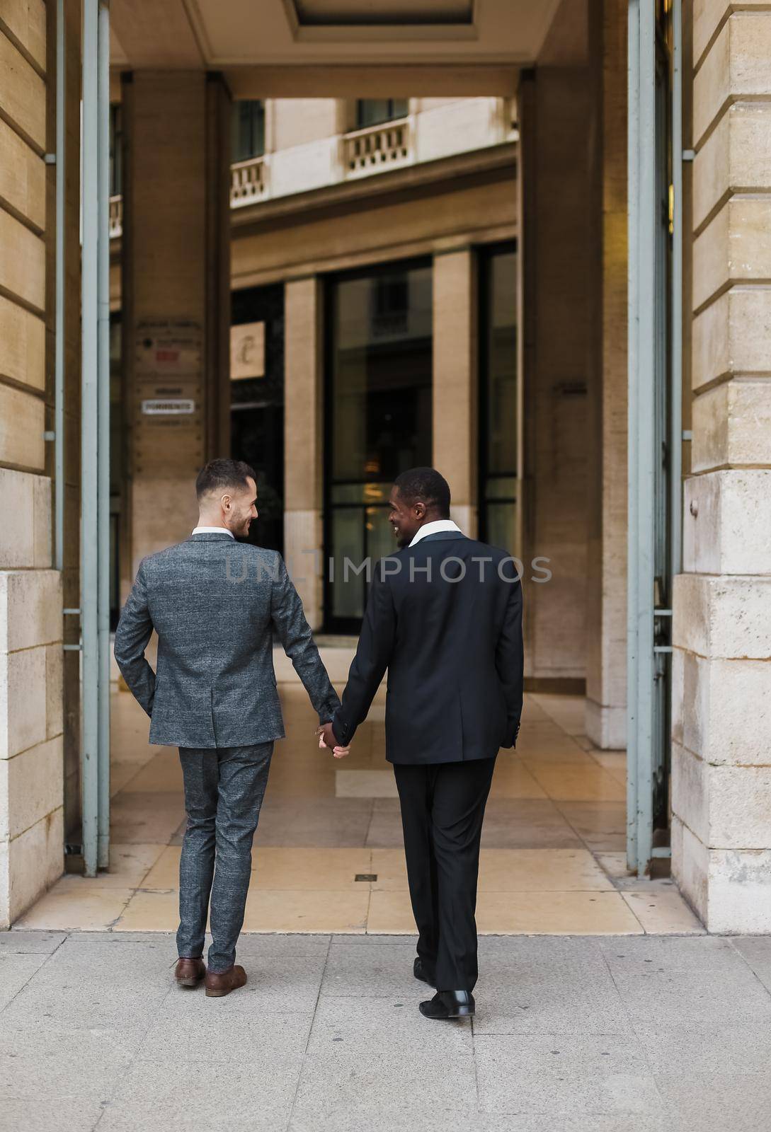 Two men, caucasian and afro american, wearing suits talking near building outside and hugging.