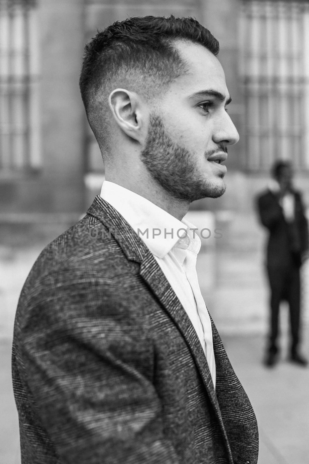 Black and white bw portrait in Paris. Young cacuasian male person wearing suit and wite shirt standing near building outdoors. Concept of fashion and businessman, urban life.