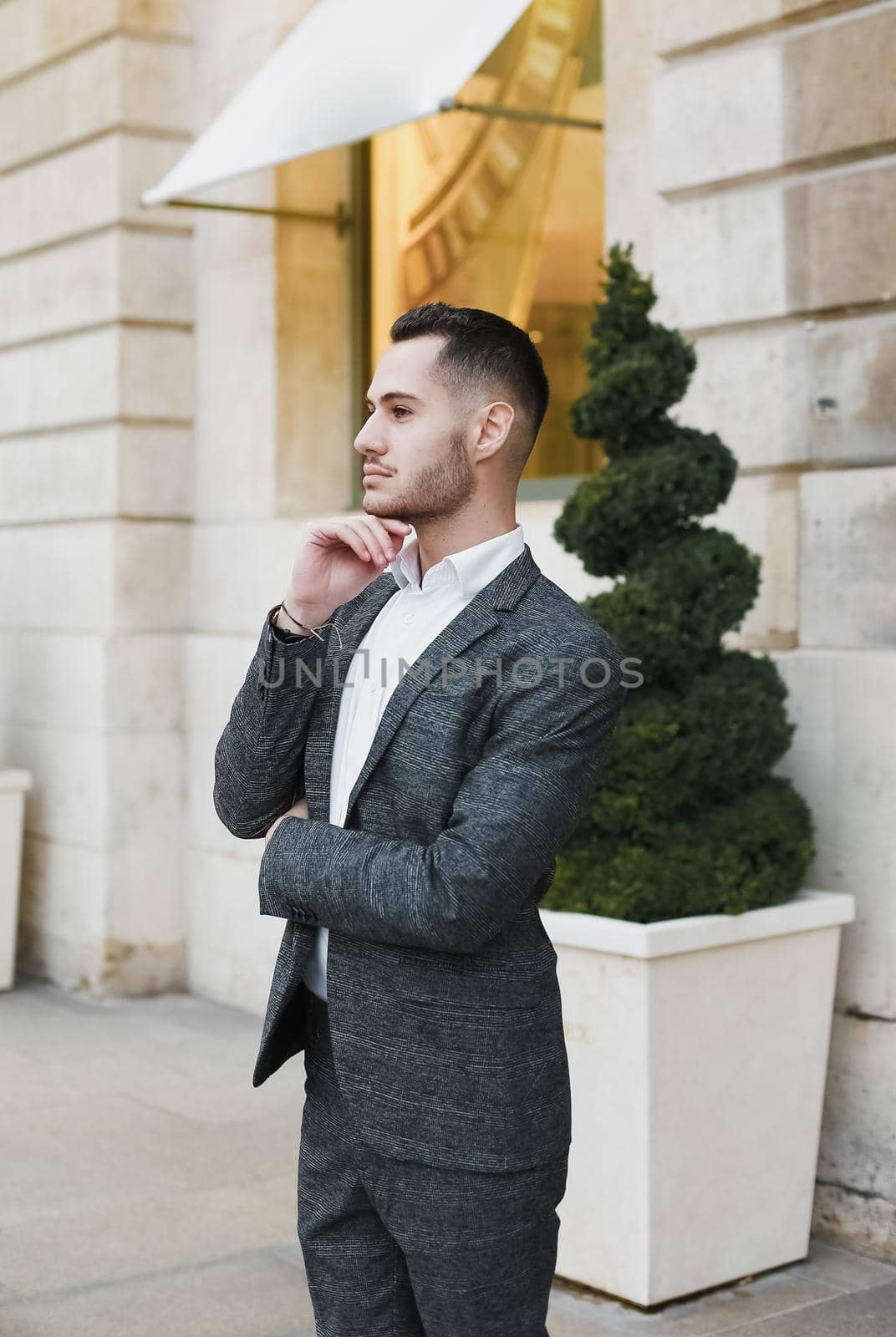 Young cacuasian male person wearing suit standing near building outdoors. Concept of fashion and businessman, urban life.