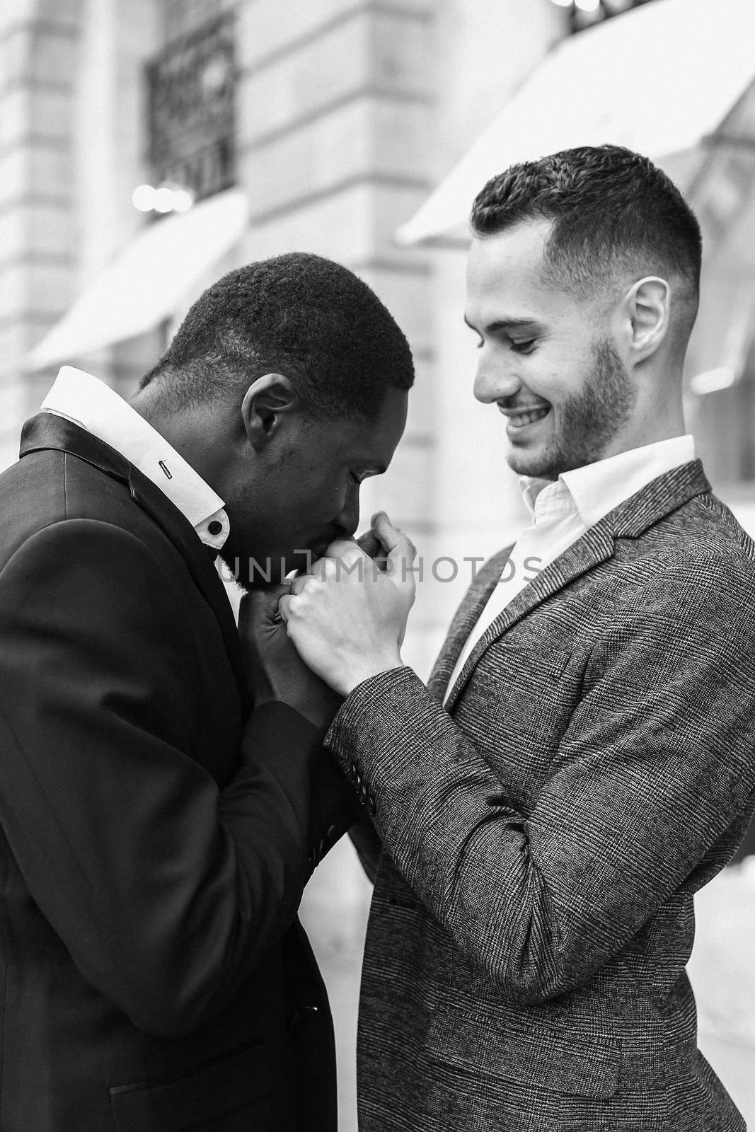 Afro american gay kissing caucasian boy outside, wearing suits. Concept of lgbt and same sex couple. Black and white bw portrait in Paris