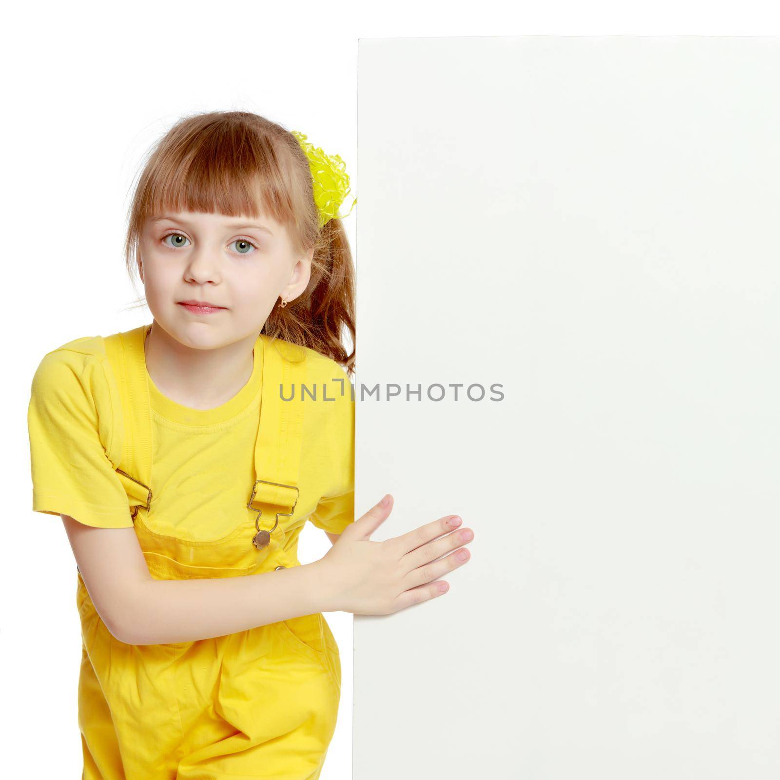 Girl with a short bangs on her head and bright yellow overalls.She crouched down on the white advertising banner.