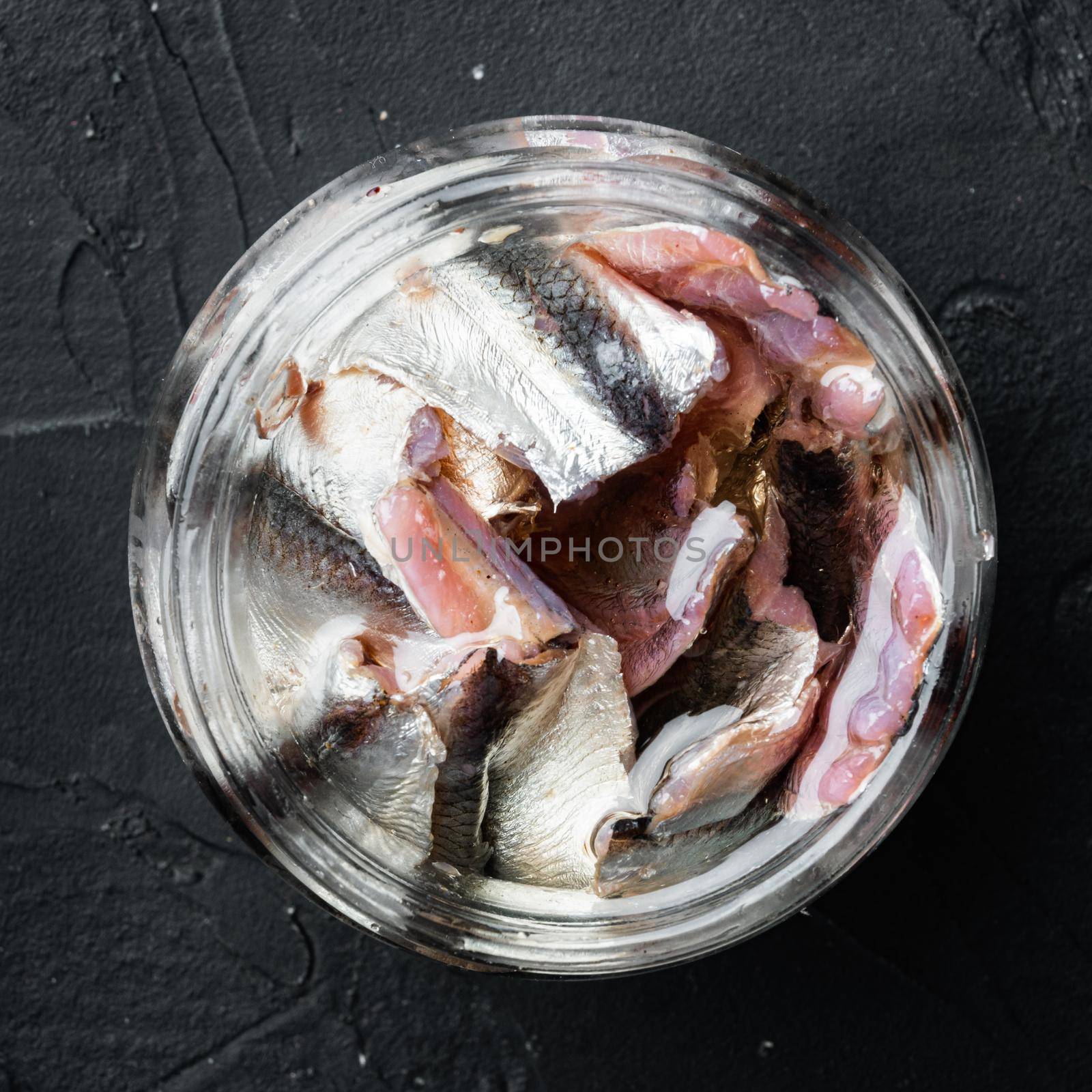 Pickled salted anchovies fillet set, in glass jar, on black background, top view flat lay, square format