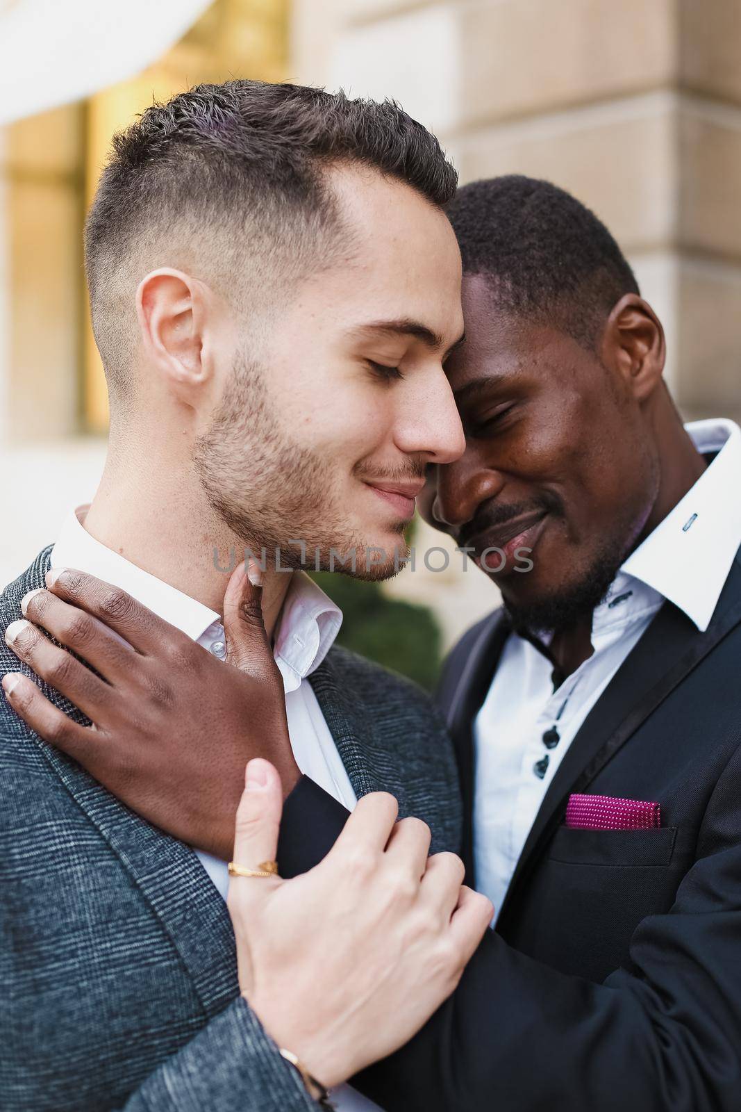 Afro american gay hugging caucasian boy outside, wearing suits. Concept of lgbt and same sex couple.