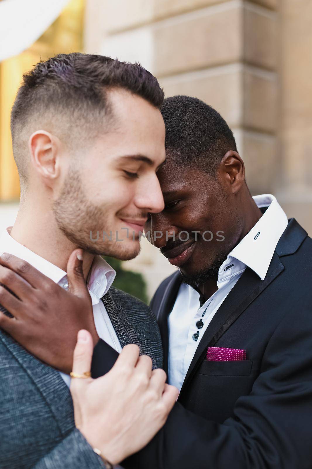 Afro american gay hugging caucasian boy outside, wearing suits. Concept of lgbt and same sex couple.