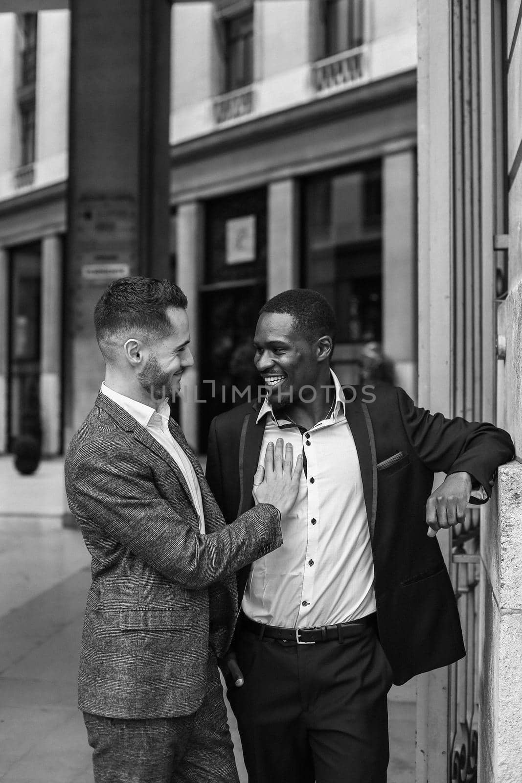 Black and white bw portrait Caucasian man hugging afro american guy outside and wearing suit. Concept of happy same sex couple and gays in Paris