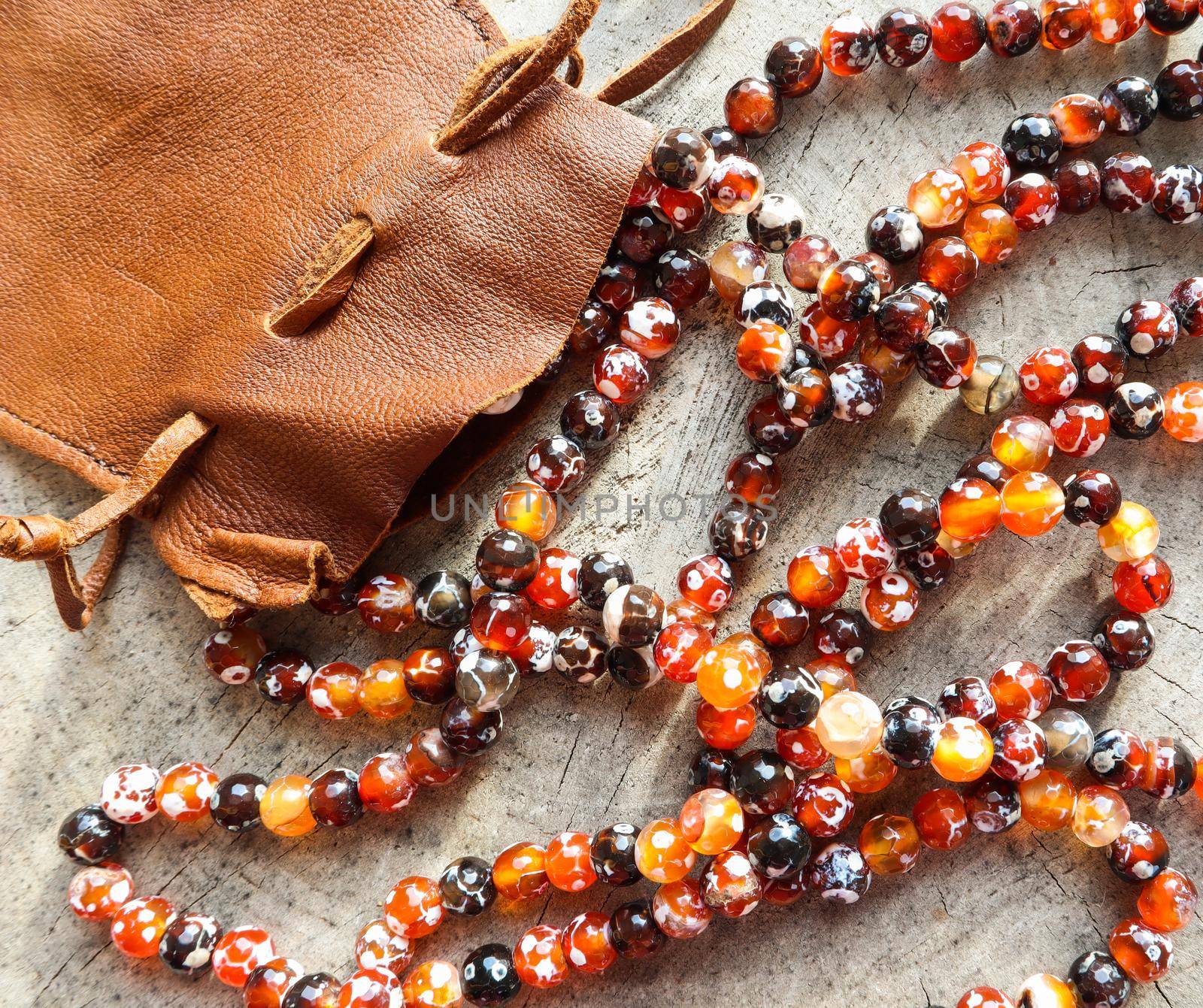 Sunny beads of amber fireplace faceted agate with leather jewelry pouch bag on rustic background by Olayola