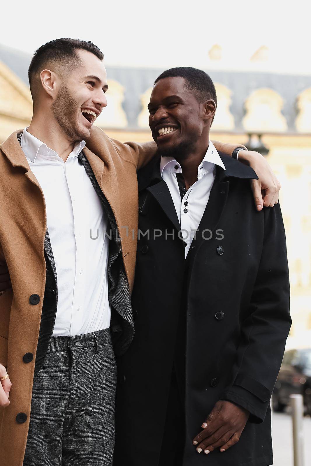 Caucasian smiling man in suit walking with afroamerican male person and hugging in city. Concept of happy lgbt gay and strolling.