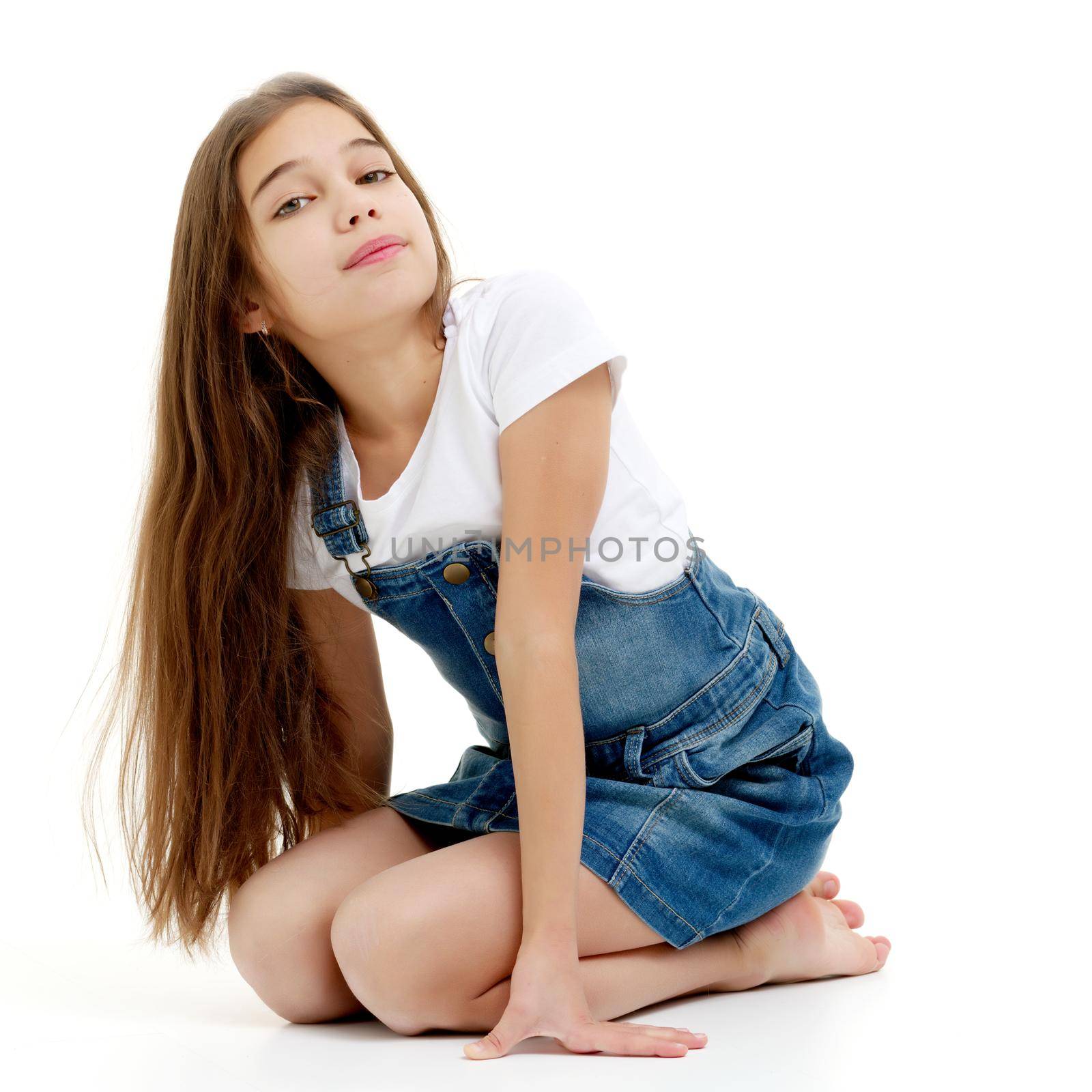 Beautiful little girl in a short denim dress. Concept of beauty and fashion, happy childhood. Isolated on white background.