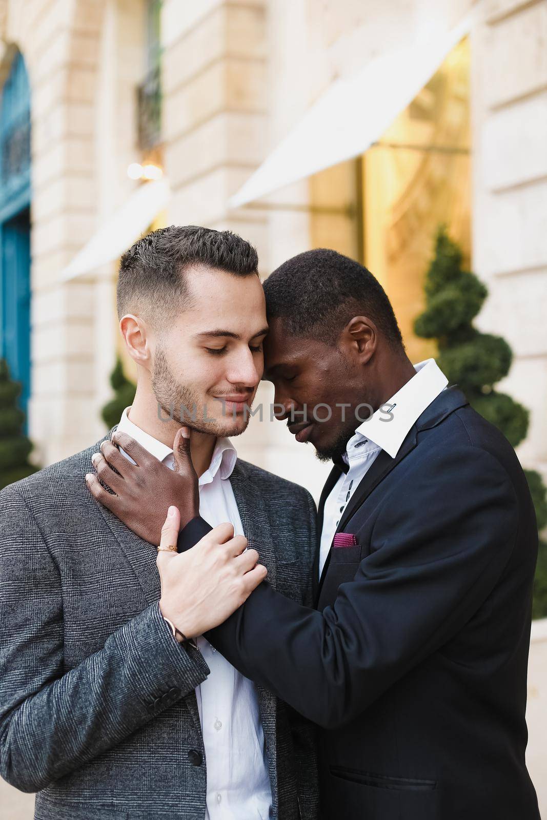 Afro american gay hugging caucasian boy outside, wearing suits. Concept of lgbt and same sex couple.