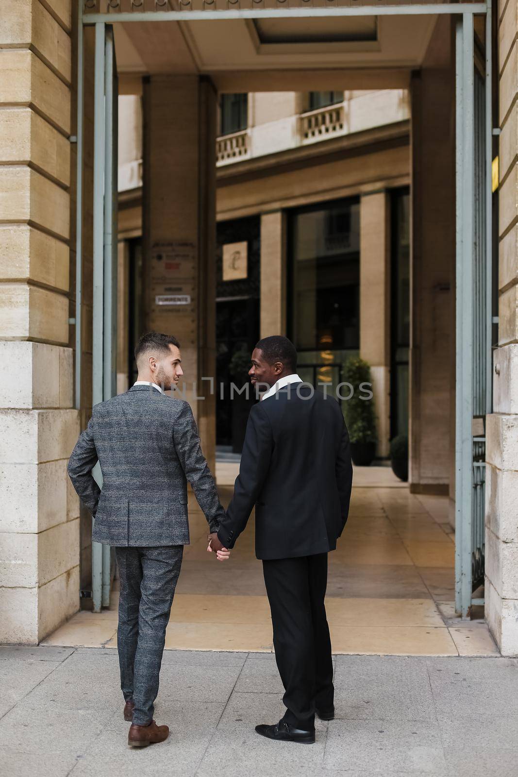 Two men, caucasian and afro american, wearing suits talking near building outside and hugging. by sisterspro