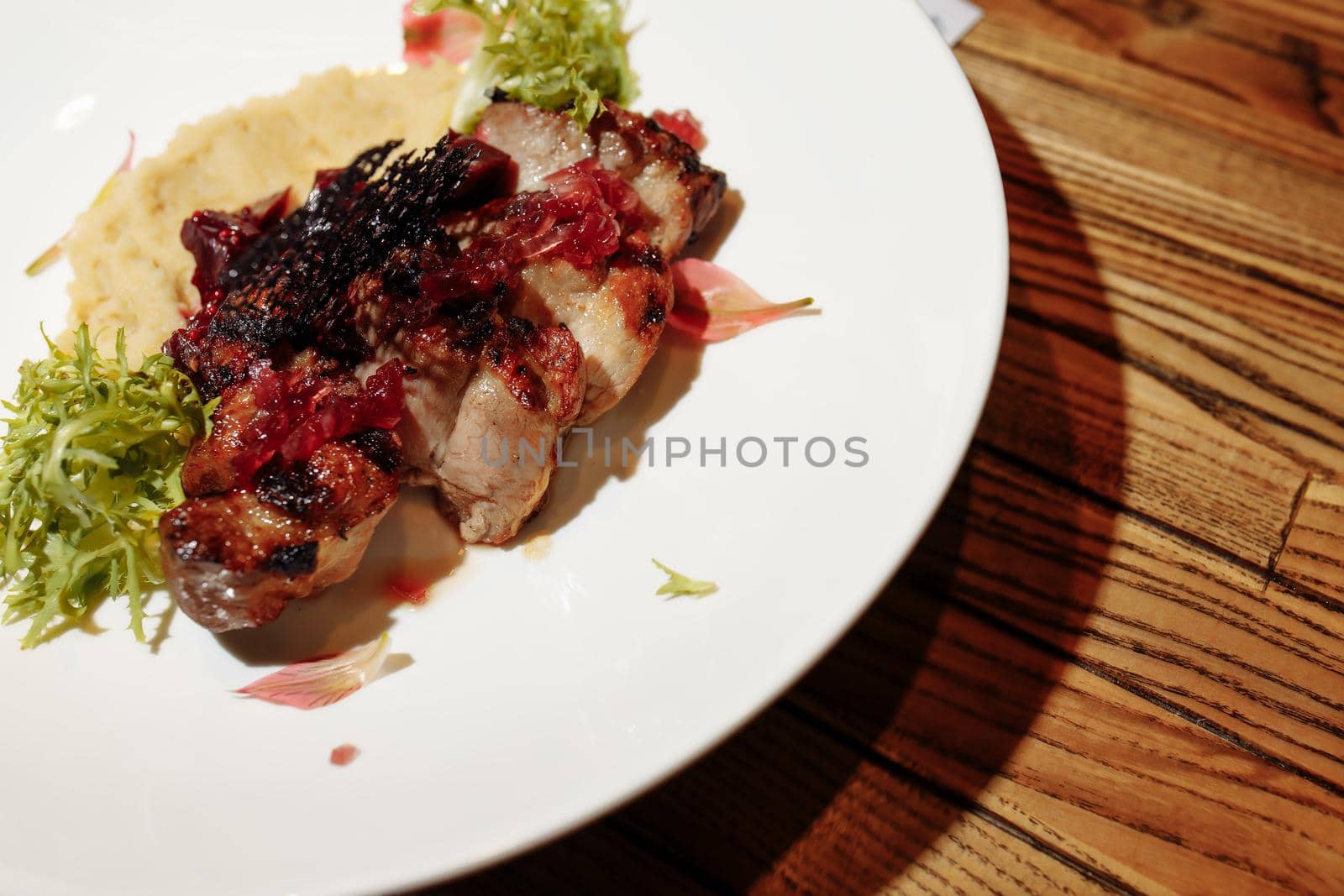 Grilled pork steak with green salad on a wooden table, top view.