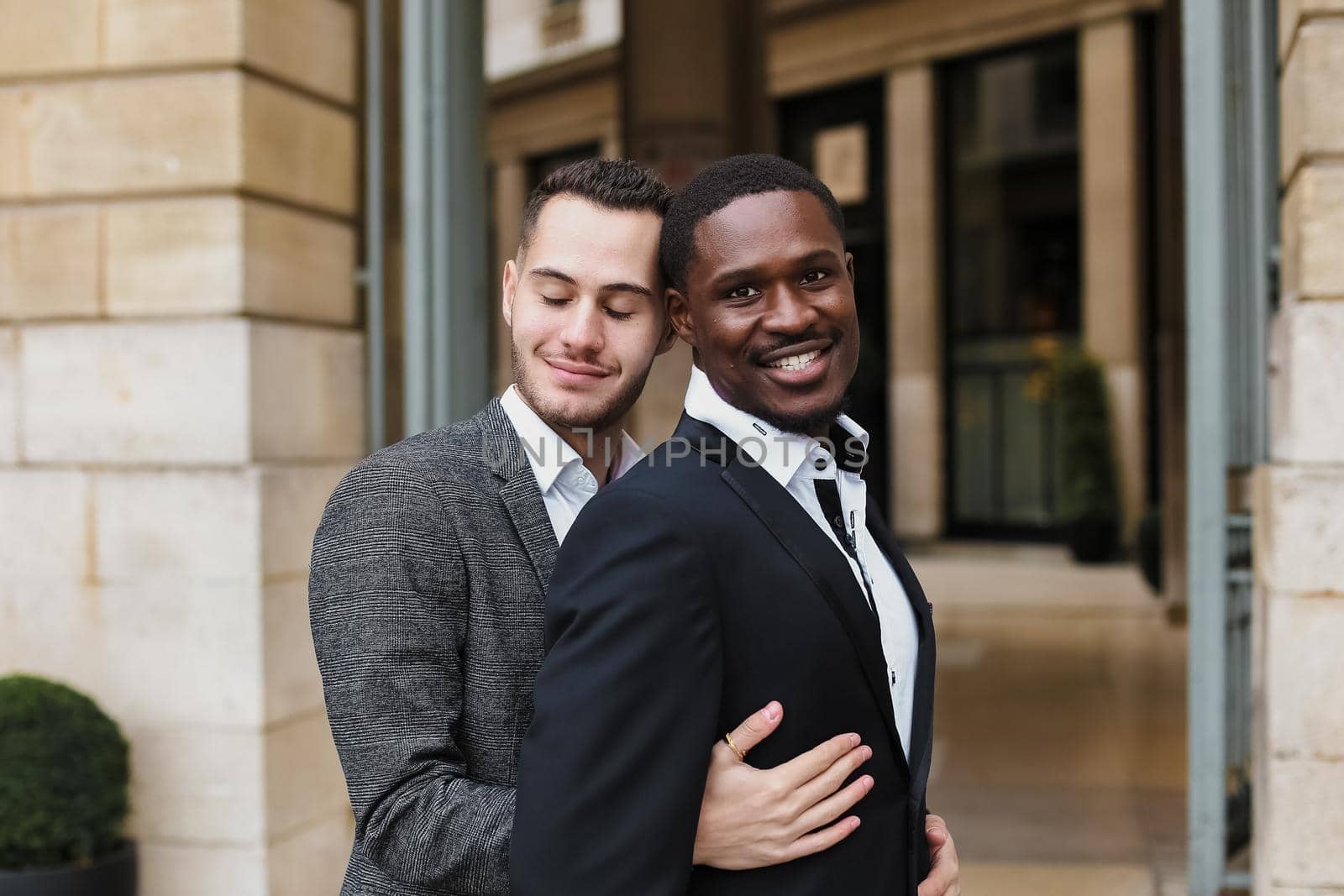 Caucasian man hugging afro american guy outside and wearing suit. Concept of happy same sex couple and lgbt gays.
