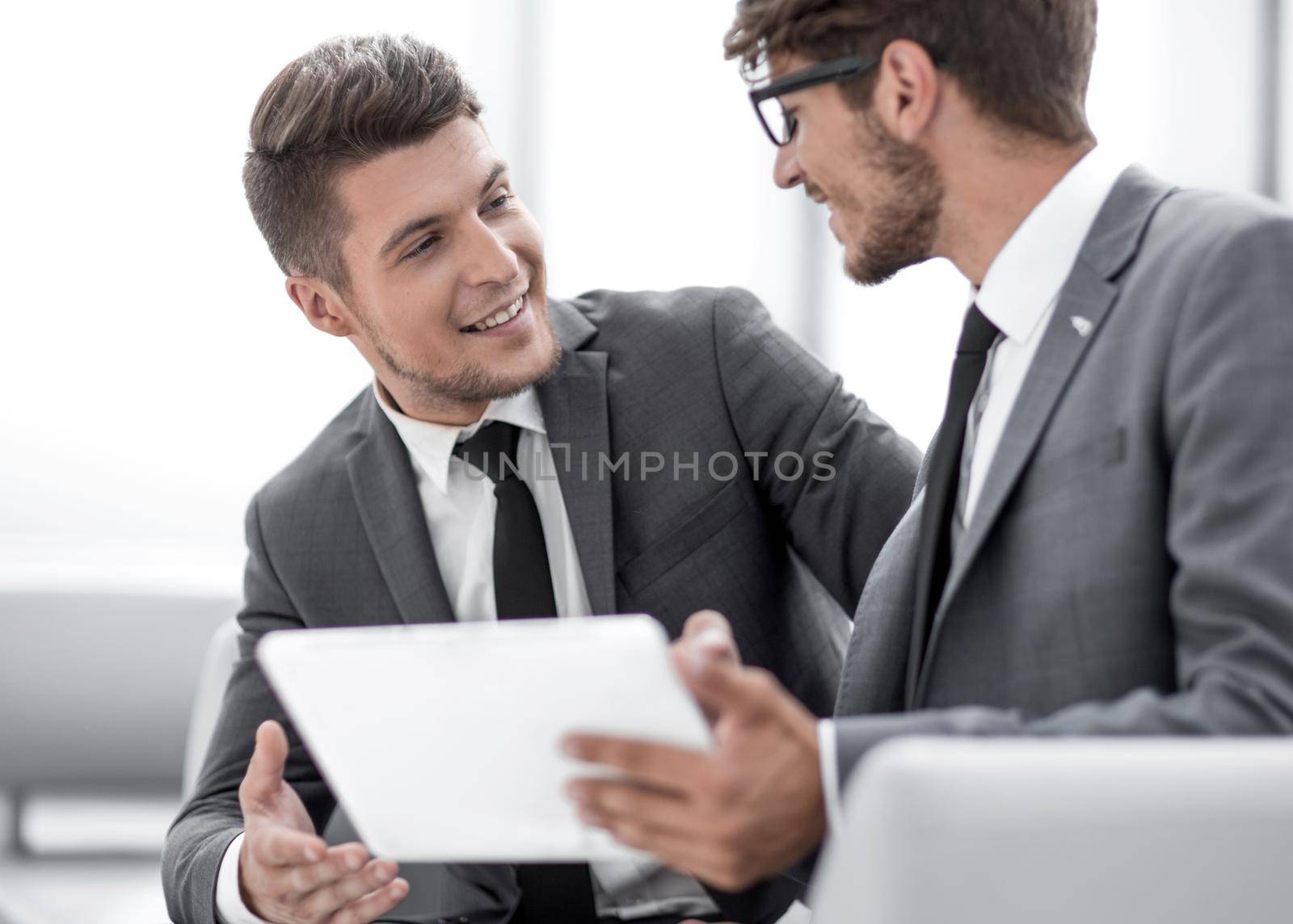 Smiling young businessman discussing something positive with his colleague, and using a digital tablet together