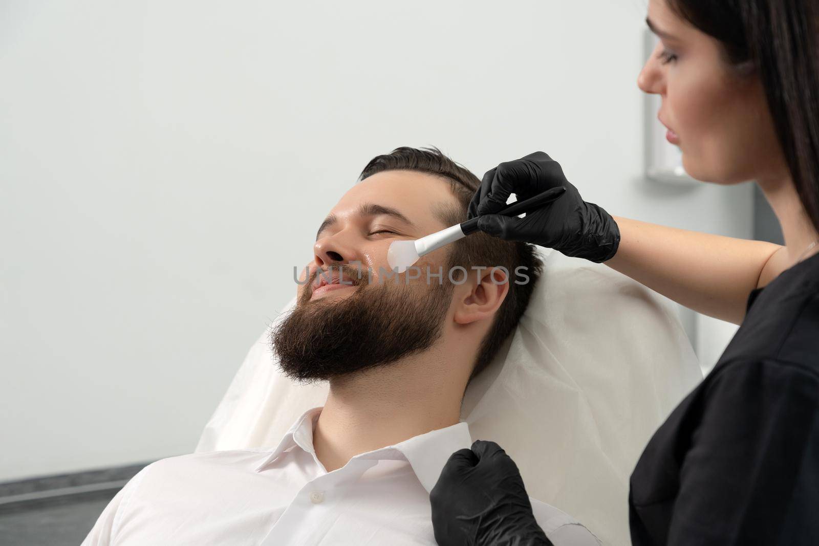 Bearded man getting laser facial treatment by professional cosmetologist in beauty clinic. Healthy man lifestyle concept