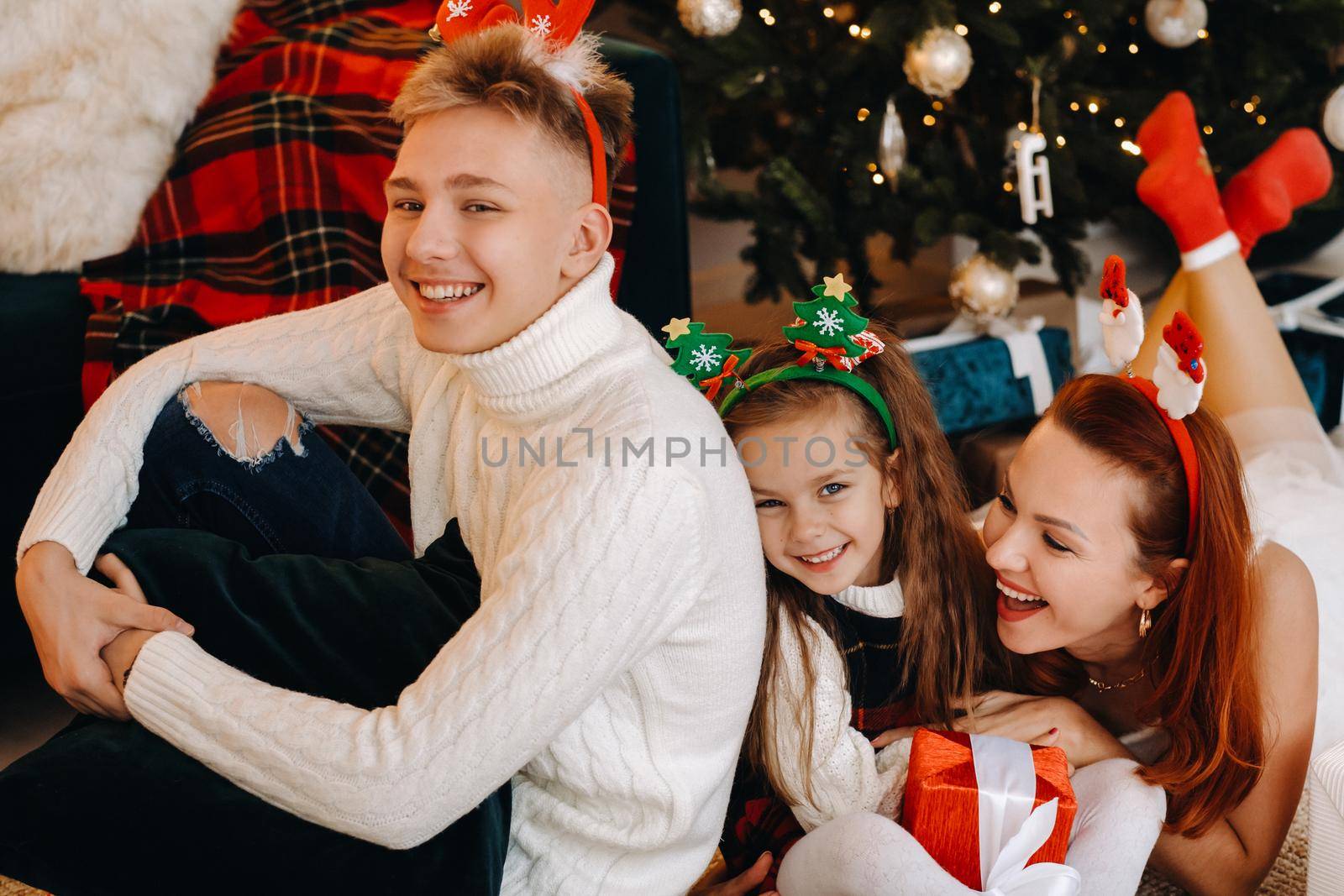 a happy family is lying on the floor of the house with New Year's gifts, next to the Christmas tree,