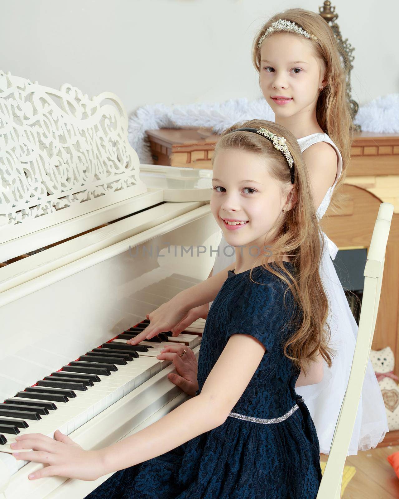Adorable little twin girls playing on a white piano near the Christmas tree.