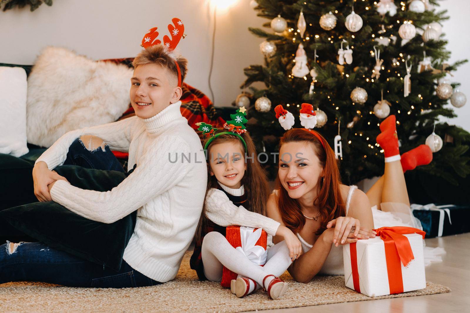 a happy family is lying on the floor of the house with New Year's gifts, next to the Christmas tree,