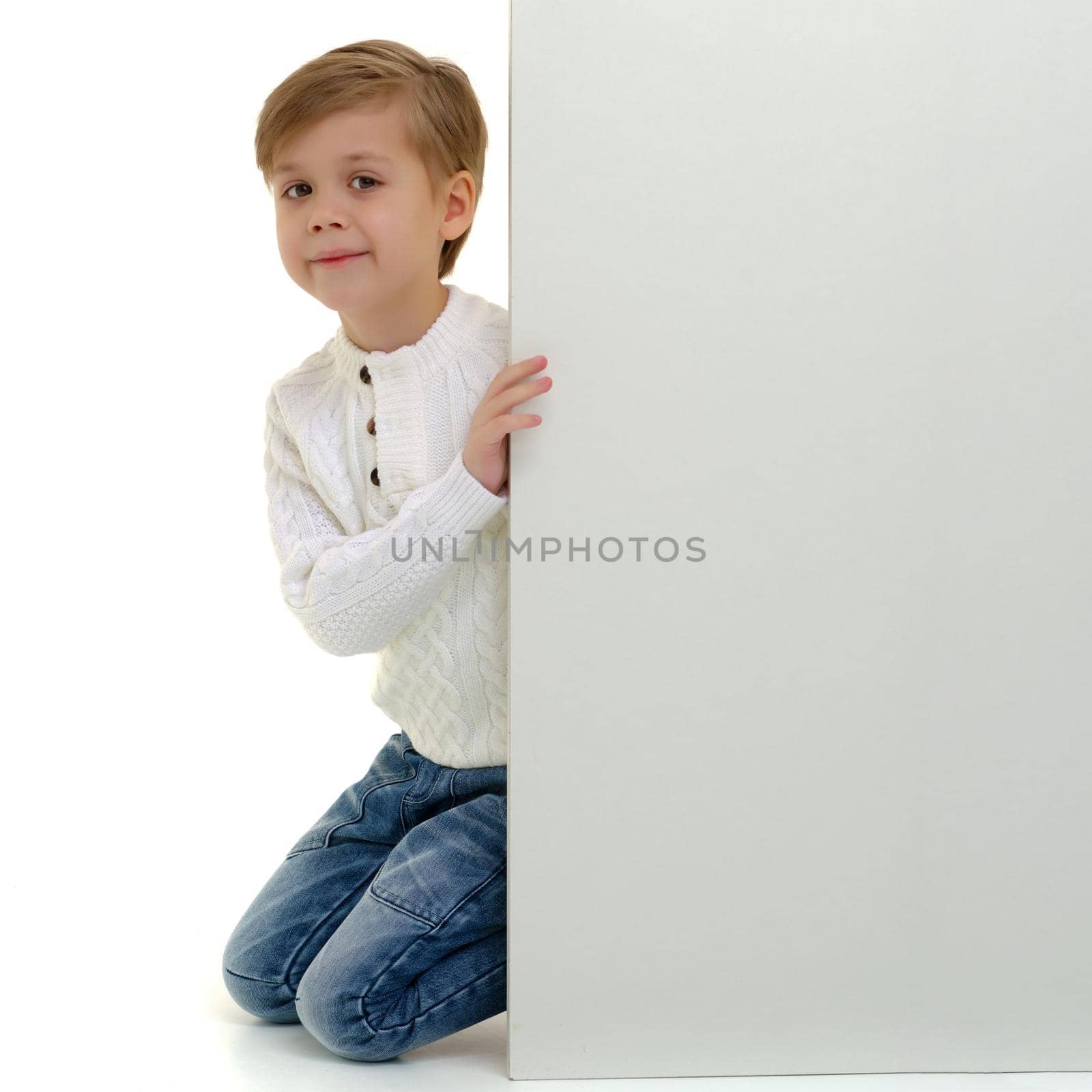A little boy looks through an empty banner on which you can write any text. The concept of a happy childhood and advertising of children's goods. Isolated on white background.