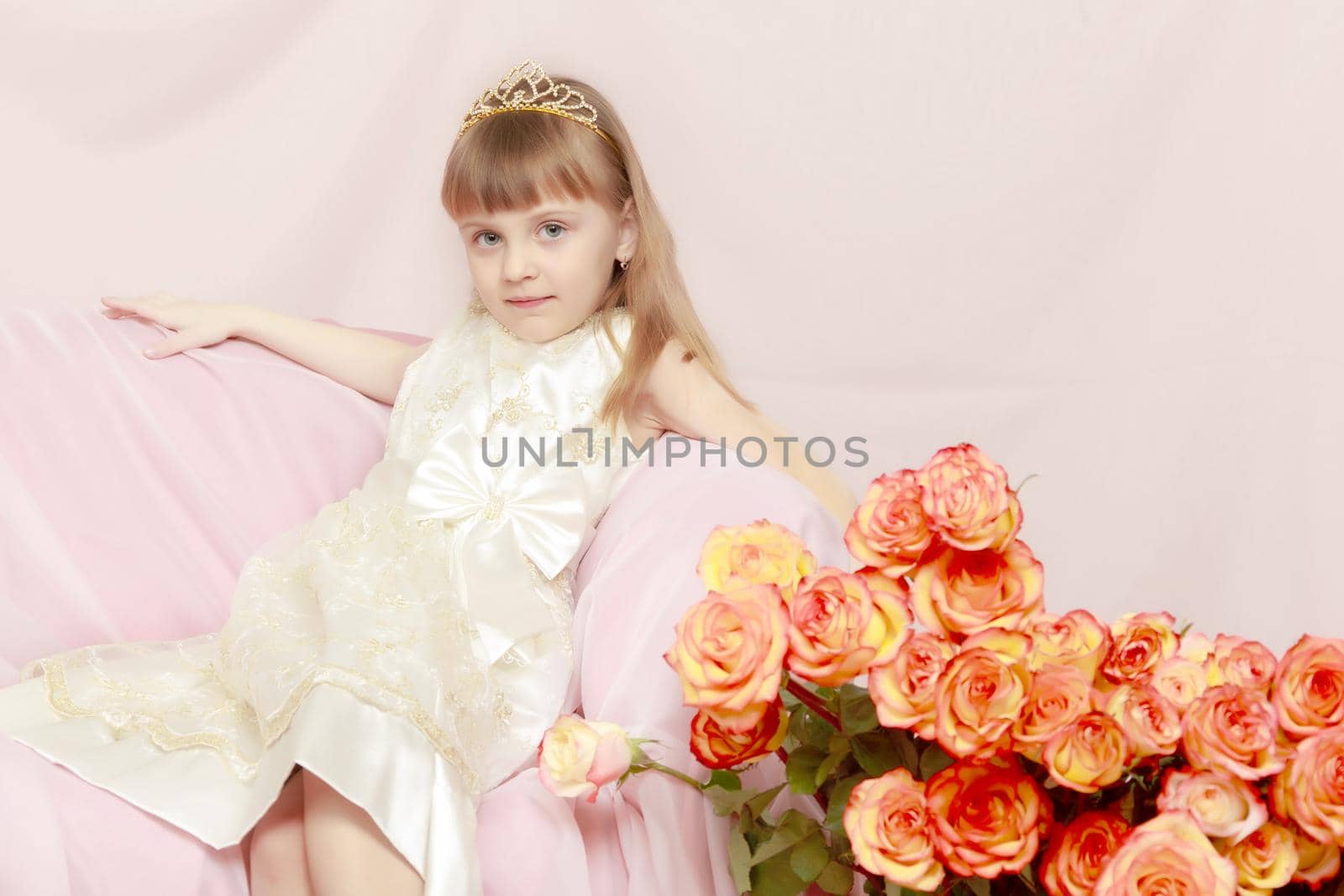 A beautiful little princess with long, light, flowing hair, in an elegant long white dress.With a bouquet of beautiful tea roses.