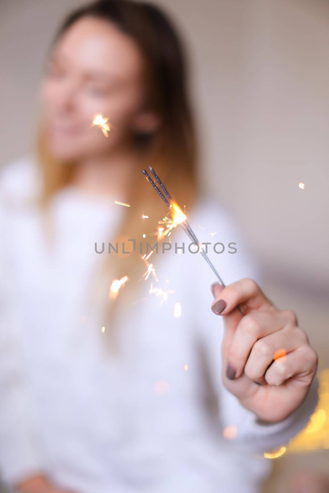 Blurred photo of american happy woman sitting with closeup bengal light near twinkling yellow garlands. Concept of handmade decorations for Christmas and New Year holidays.