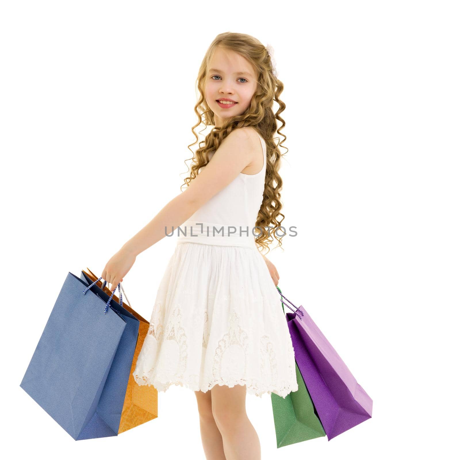 A cheerful little girl is shopping in a store with large, multi-colored paper bags. The concept of holidays, advertising sales. Isolated on white background.