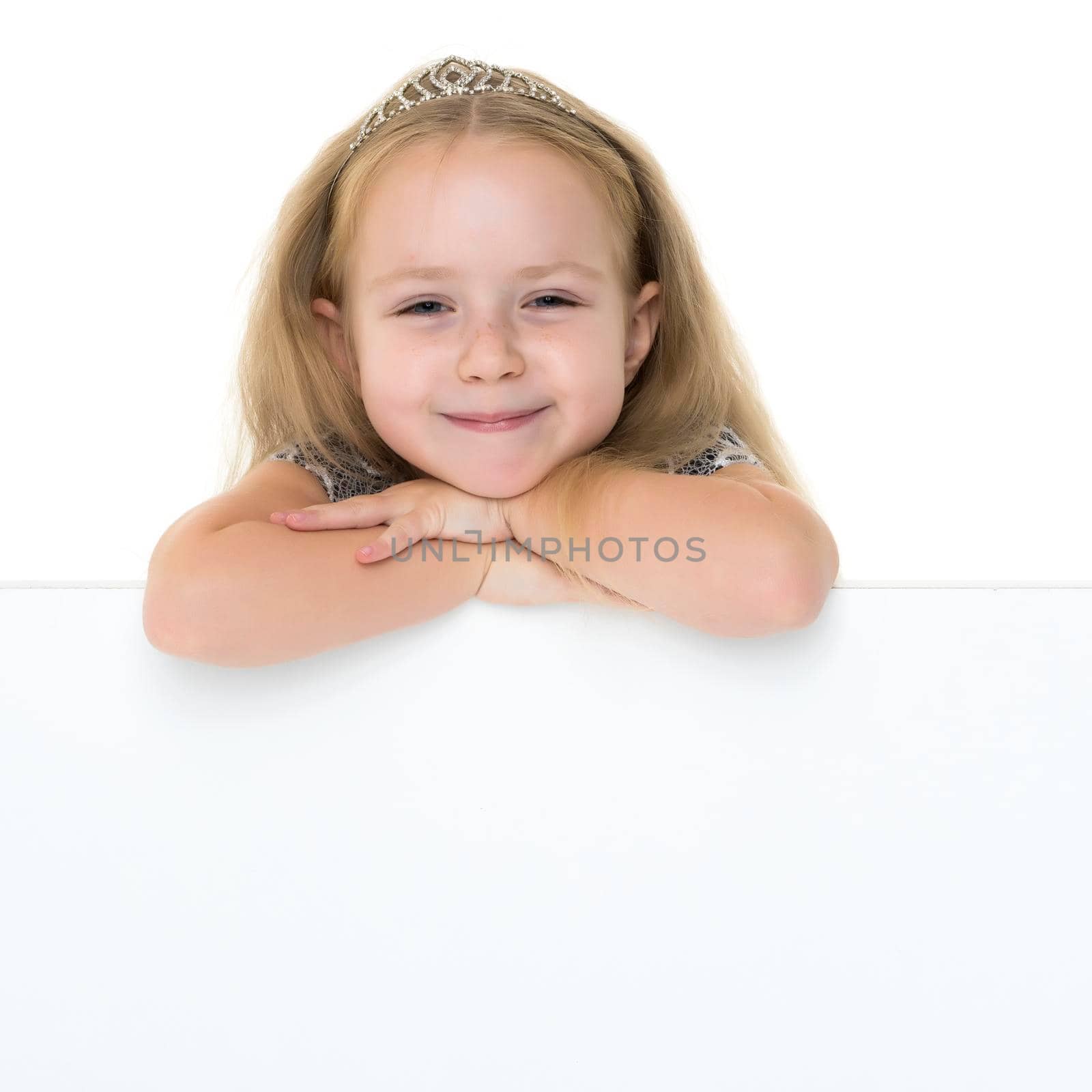 A nice little girl is looking because of an empty banner in which you can insert any text. The concept of a happy childhood, advertising, selling goods. Isolated on white background.