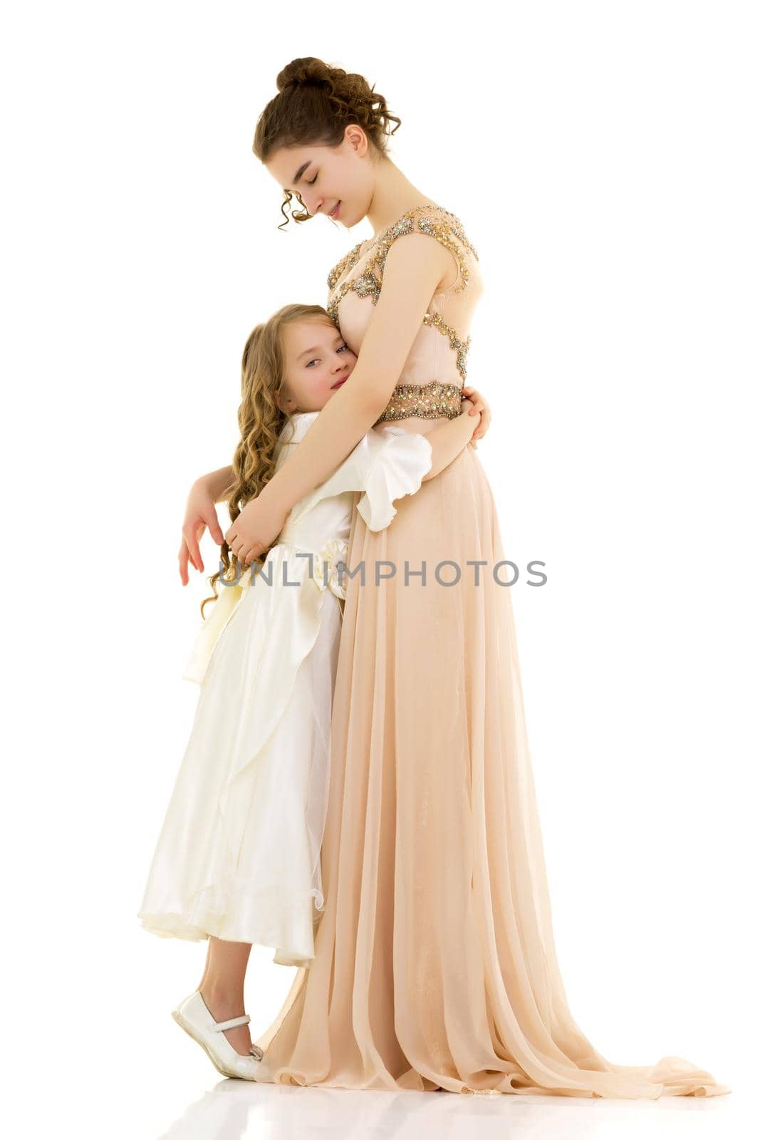 Beautiful young girl hugging her little sister. The concept of a happy childhood, family values. Isolated on white background.