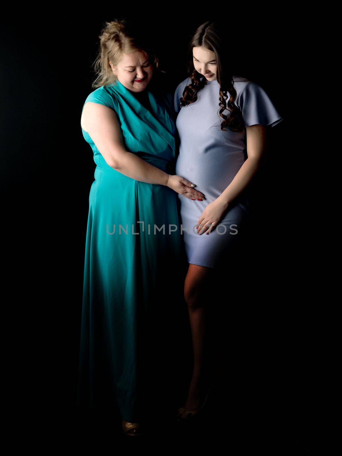 Young pregnant girl with mother on a black background.