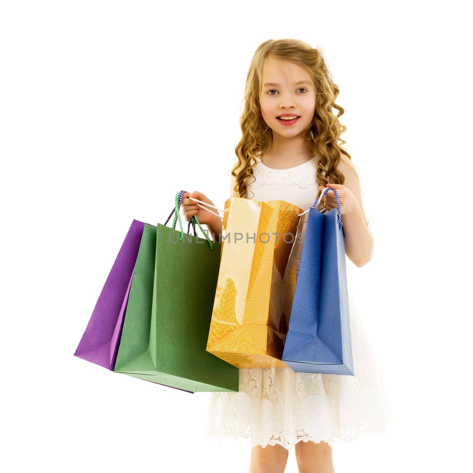 A cheerful little girl is shopping in a store with large, multi-colored paper bags. The concept of holidays, advertising sales. Isolated on white background.