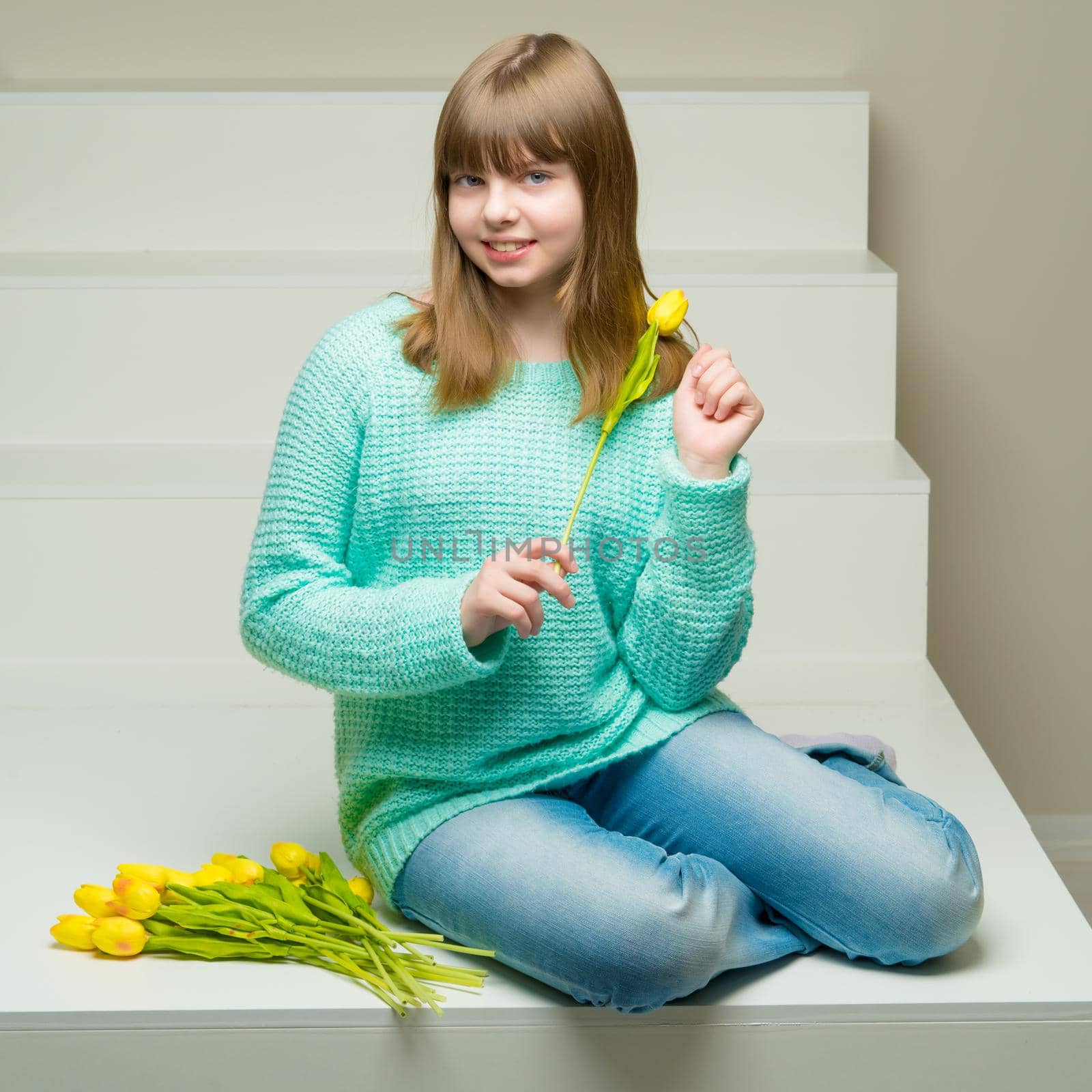 A cute little girl with a bouquet of tulips sits on a white staircase. The concept of happy people, spring mood.