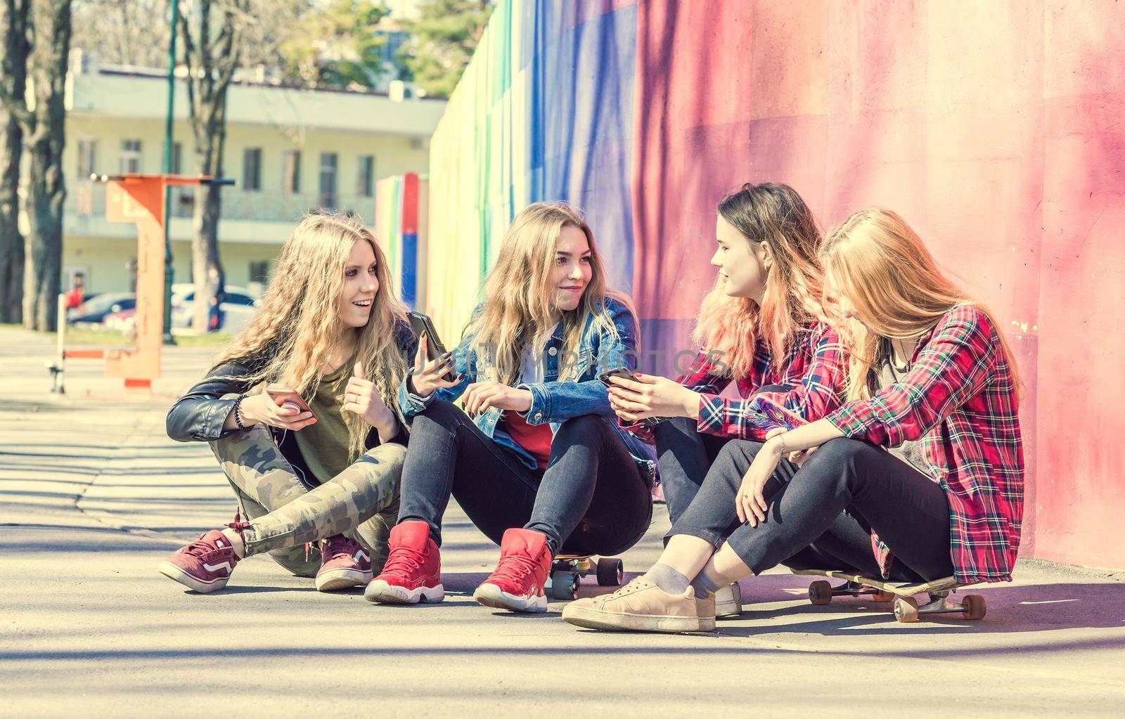 Four cool teenage girls with smartphones in the park