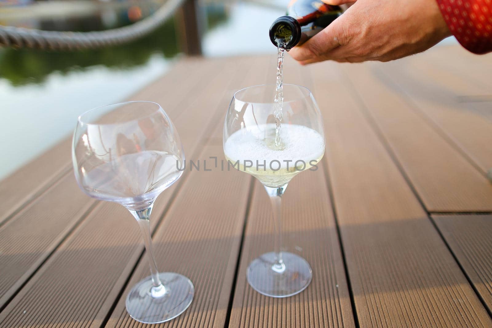 Male hands wearing red shirt pouring wine on wooden table. Concept of sommelier profession and alcohol.