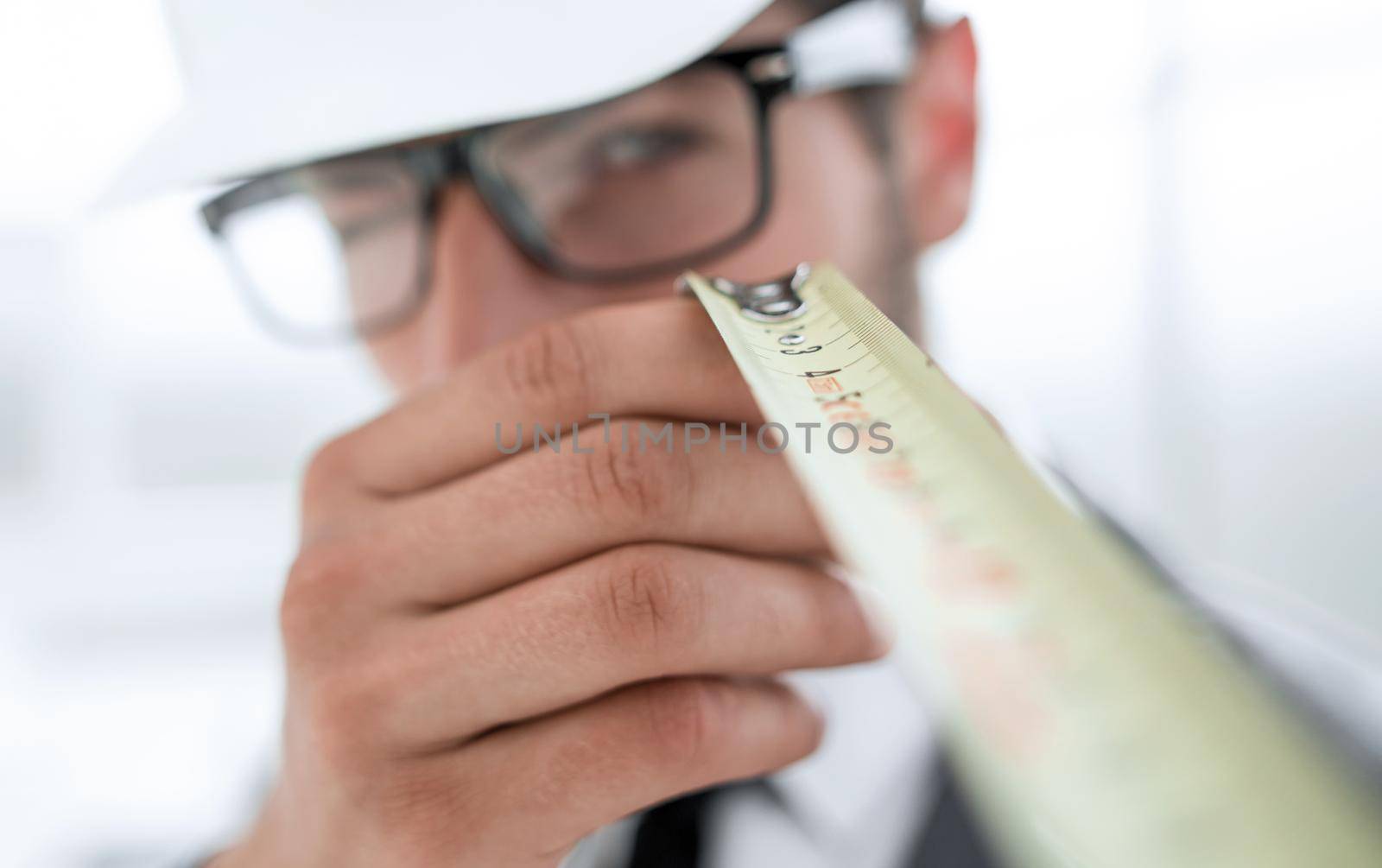 Builder. Mechanic in construction helmet holds construction ruler near face. Man with construction roulette.