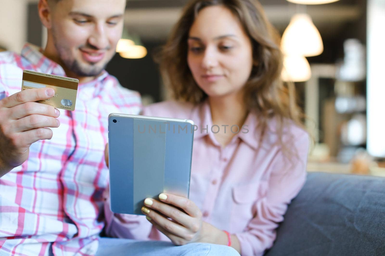 Young wife and husband using tablet and debit card at cafe. Concept of purchasing online and shopping, modern technology.