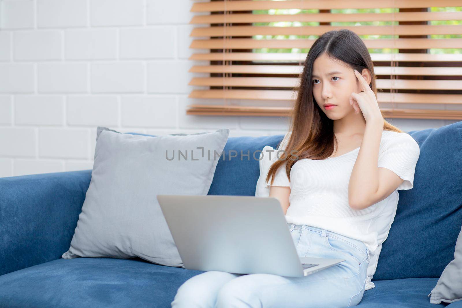 Young asian woman work on laptop computer on sofa at home with frustrated and bored, freelance girl unhappy and tired with unsuccessful, upset from problem, failure and mistake, business concept.