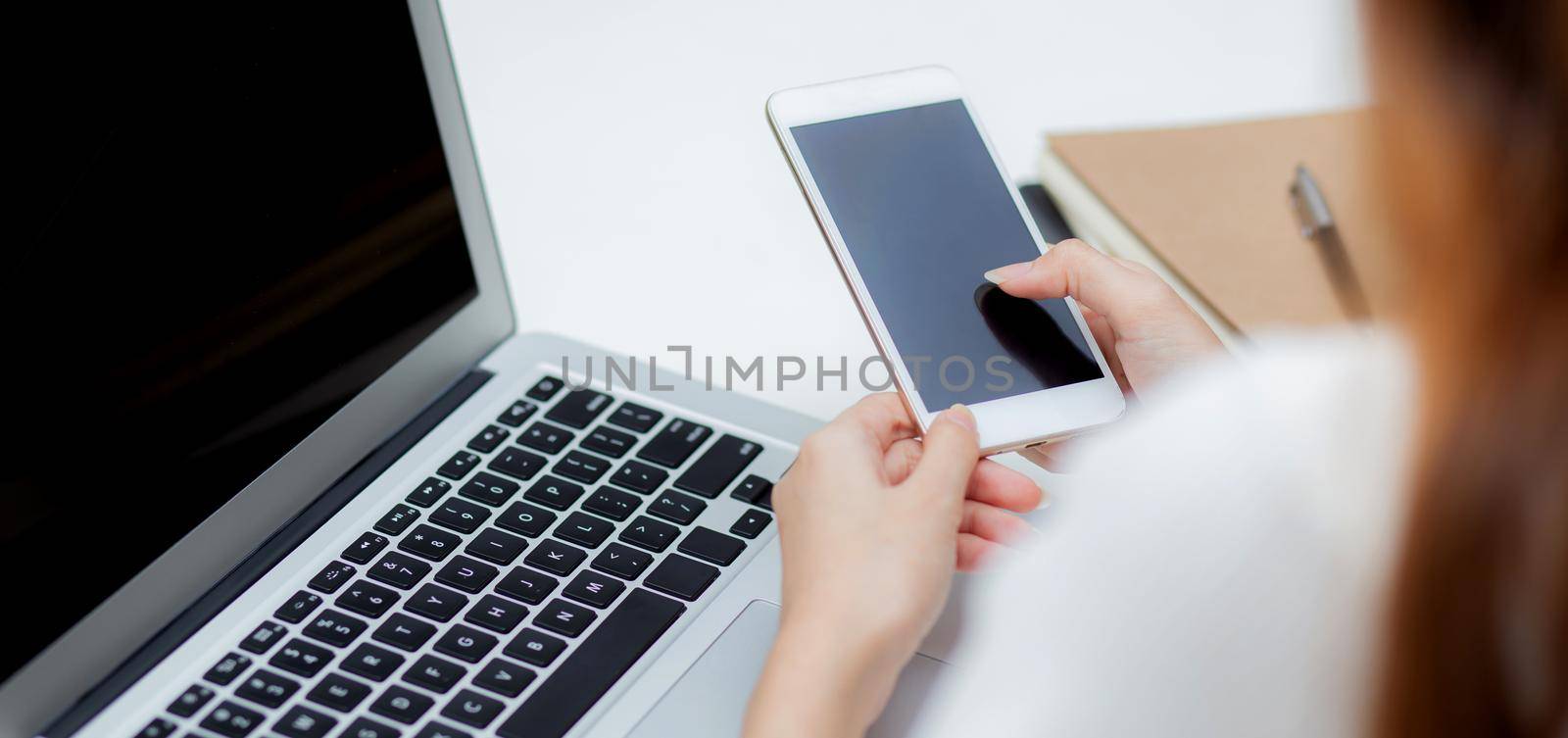 Hand of young woman working with laptop computer and smartphone mockup on desk at home, notebook and phone display blank screen, freelance look message to internet, business and communication concept.