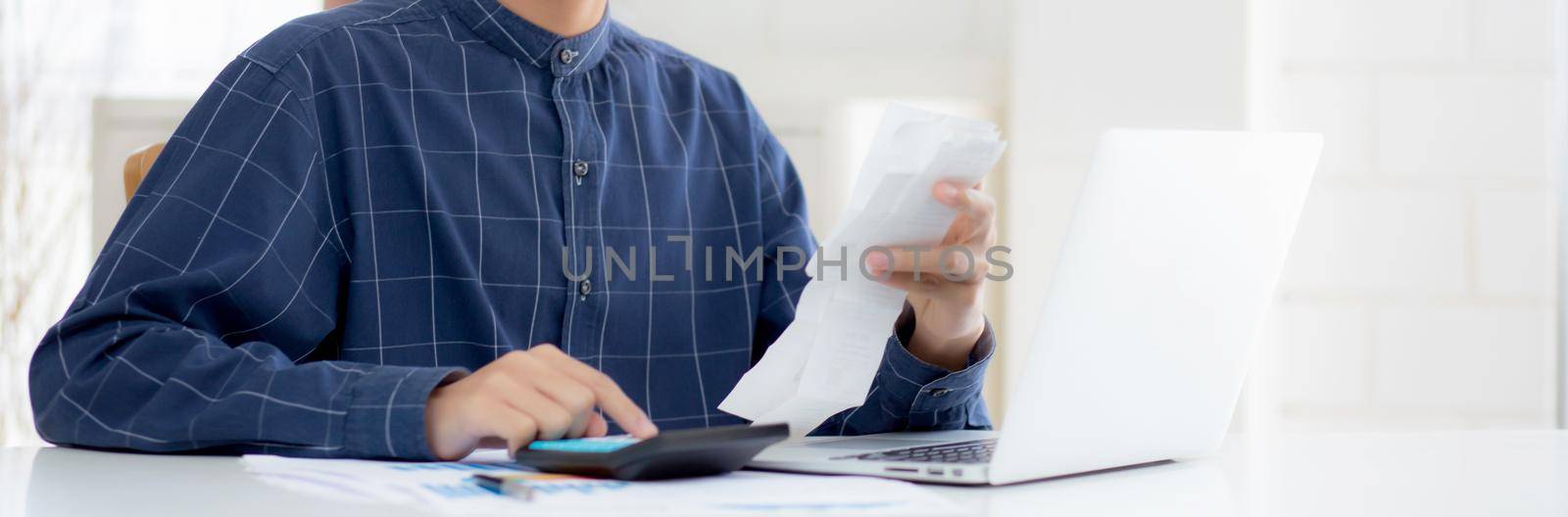 Young asian man calculating finance household with calculator on desk at home, male checking bill and success for saving expenses household, debt closure, tax and accounting, business concept. by nnudoo