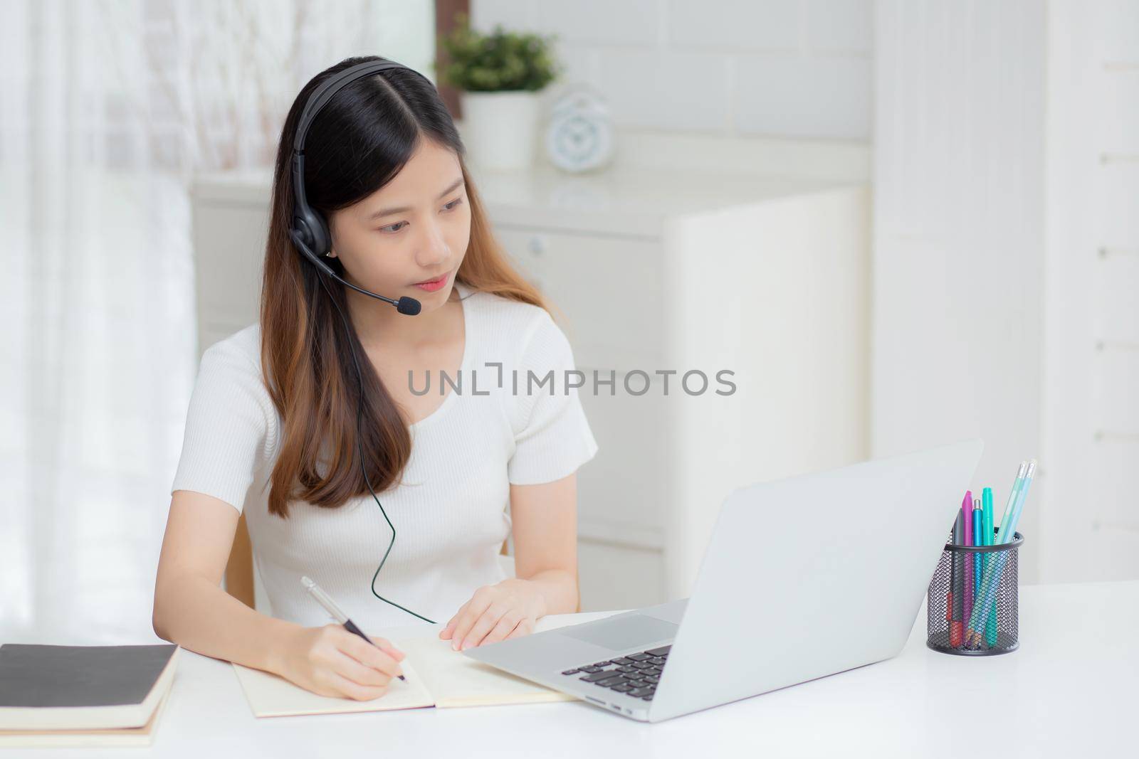 Young asian woman wearing headphone study online with e-learning on desk, girl wearing headset learning to internet with laptop computer at home, new normal, distance education and training.