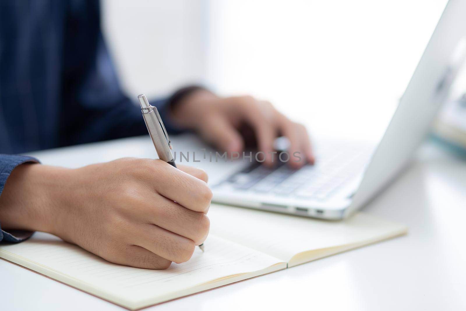 Closeup hand of business man writing on note while using laptop computer on desk at home, male planning on note for business success, author and blog, businessman working on table, employee and job.