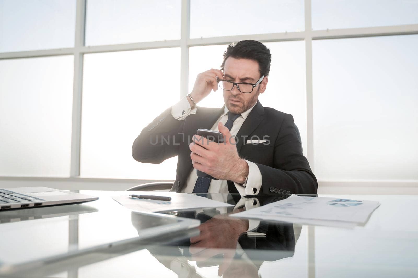 businessman using smartphone sitting at his Desk by asdf